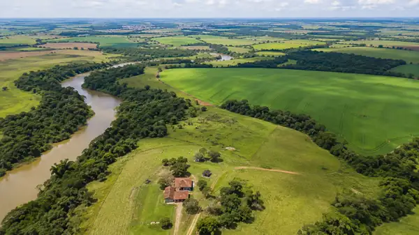 Vista aérea de propriedade rural brasileira com rio, campos verdes e floresta