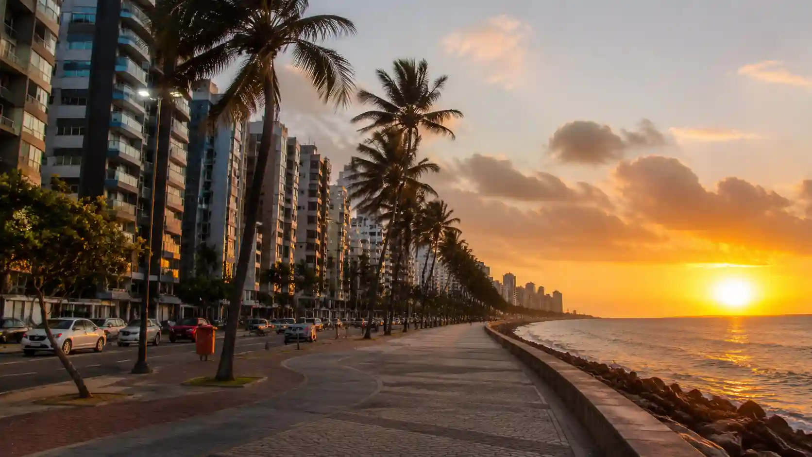 Calçadão de Boa Viagem Recife ao entardecer com edifícios modernos e coqueiros